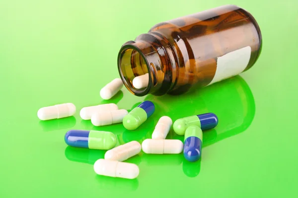 Pill bottle with white and blue pills on green — Stock Photo, Image