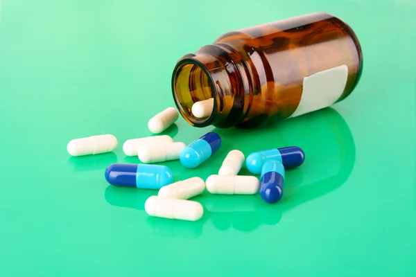 Tablettenflasche mit farbigen Pillen auf grün — Stockfoto