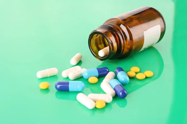 Pill bottle with coloured pills on green — Stock Photo, Image