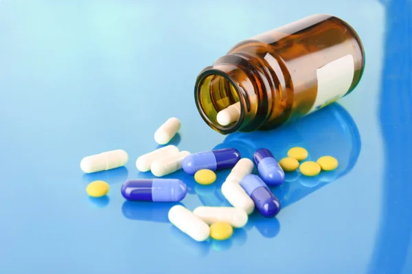 Tablettenflasche mit farbigen Pillen auf blau — Stockfoto