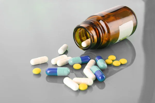 Pilulku láhev s barevnými prášky na šedé backlround — Stock fotografie