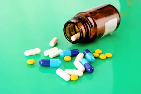 Pilulku láhev s barevnými prášky na zelené — Stock fotografie