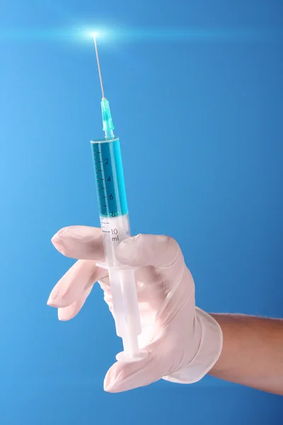 Syringe in doctors hand over blue background Stock Picture