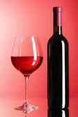 láhev vína a skla na červeném pozadí