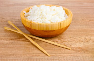 Wooden bowl of cooked rice and chopsticks on wooden table