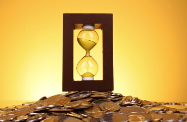 Hourglass and coins on yellow background clipart