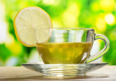 Tea with lemon on green leaves background clipart