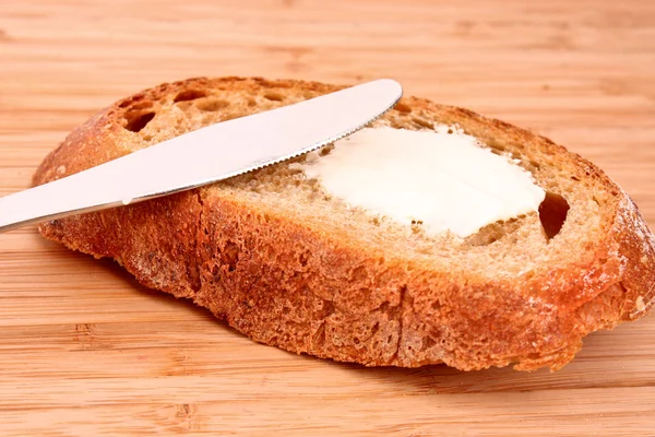 Knife and a bread with butter on a wooden stand — Stock Photo, Image