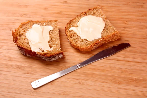Kinfe e pão com manteiga na superfície de madeira — Fotografia de Stock