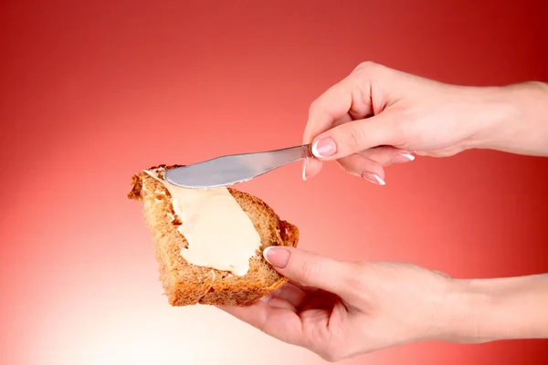 Woman hands spread bread with butter on red background — Stock Photo, Image