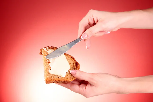 Frauenhände streichen Brot mit Butter auf rotem Hintergrund — Stockfoto