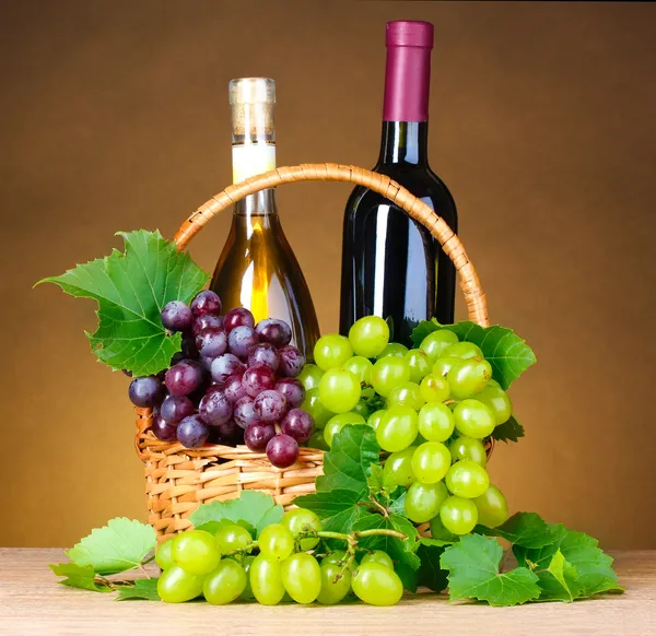 Flaskor vin och druvor i korg på gul bakgrund — Stockfoto