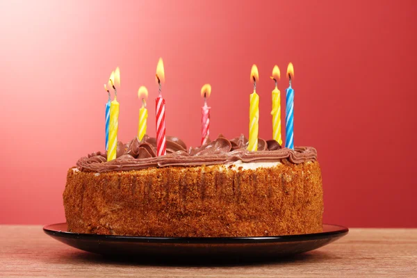 Cake met kaarsen op rode achtergrond — Stockfoto