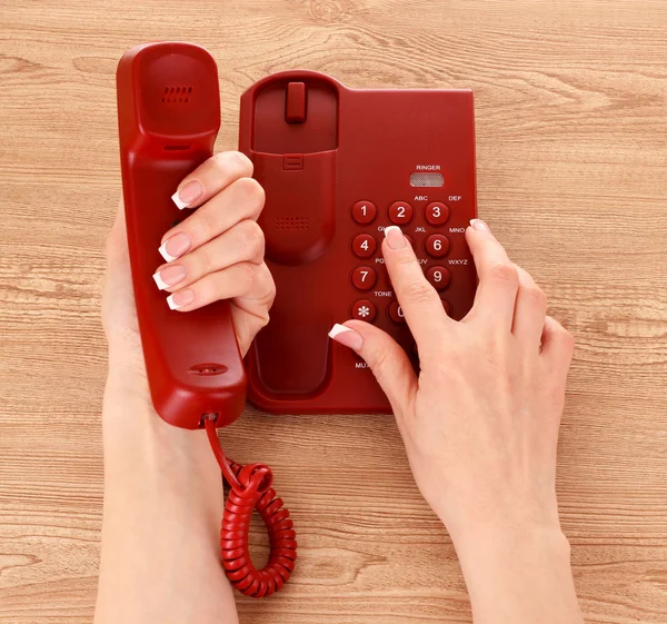 Red phone and hands on wooden table — Stock Photo, Image