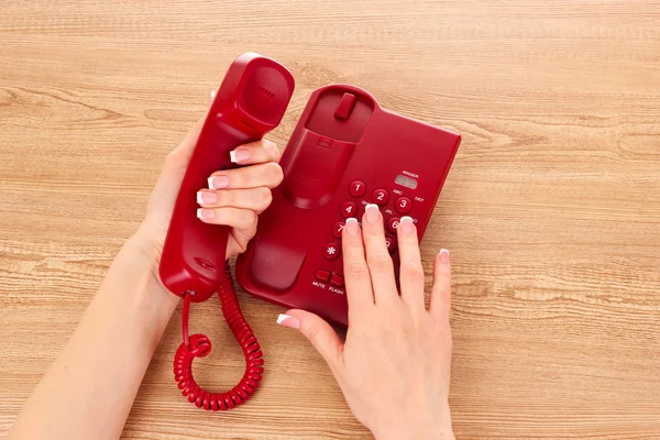 Telefone vermelho e mãos na mesa de madeira — Fotografia de Stock