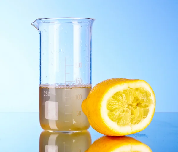 Suco em um tubo de ensaio e limão espremido em um fundo azul — Fotografia de Stock