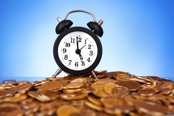 Reloj despertador con monedas de oro sobre fondo azul — Foto de Stock