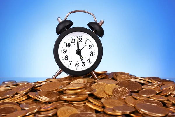 Alarm clock with golden coins on blue background — Stock Photo, Image