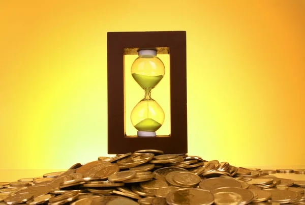 Reloj de arena y monedas sobre fondo amarillo — Stockfoto