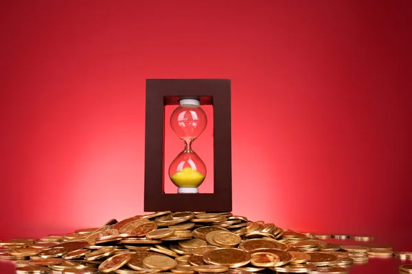 Sanduhr und Münzen auf rotem Hintergrund — Stockfoto