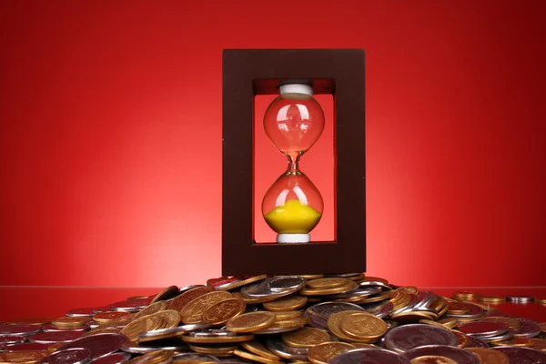 Timeglas og mønter på rød baggrund - Stock-foto