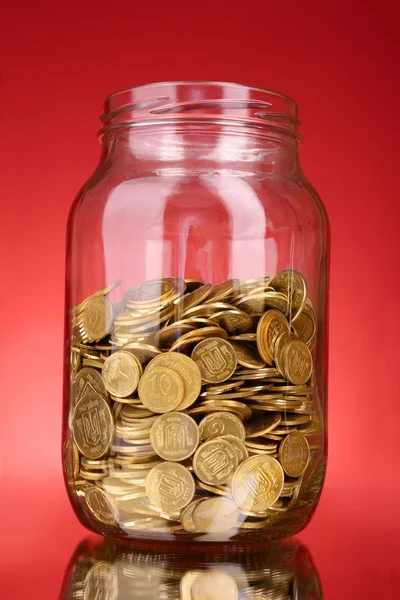 Монети в грошовій банці на червоному тлі — стокове фото