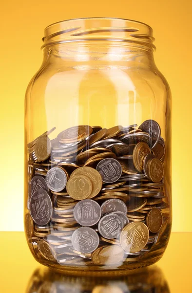 Monedas en frasco de dinero sobre fondo amarillo — Foto de Stock