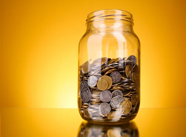 Coins in money jar on yellow background — Stock Photo, Image