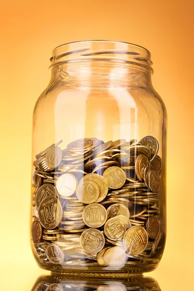 Monedas en frasco de dinero sobre fondo amarillo — Foto de Stock