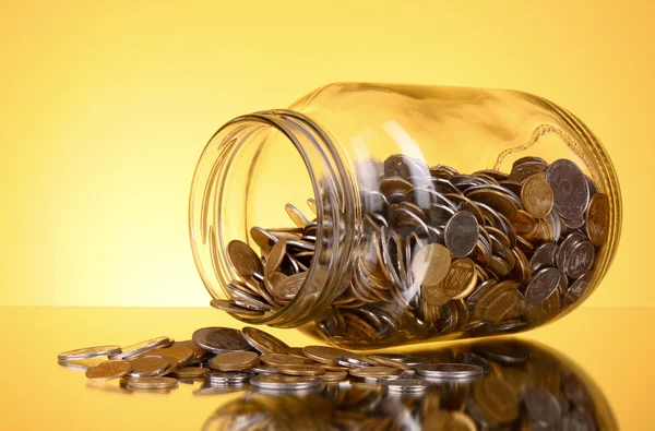 Coins spilling from a money jar on yellow background — Stock Photo, Image