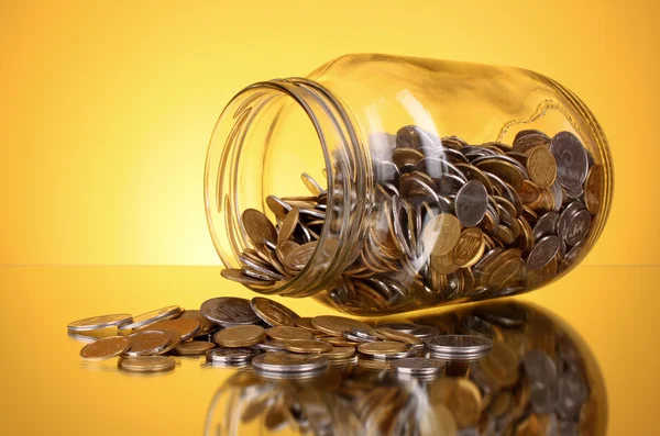 Монети, що виливаються з грошової банки на жовтому фоні — стокове фото