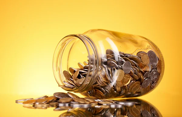 Монеты, льющиеся из банки с деньгами на жёлтом фоне. Украинский — стоковое фото