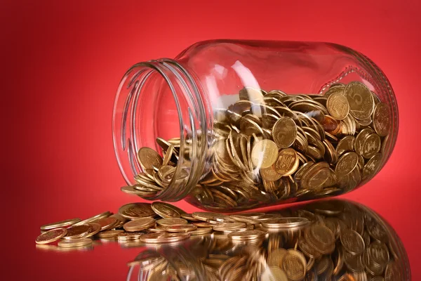 Münzen, die aus einem Geldbehälter auf rotem Hintergrund austreten — Stockfoto