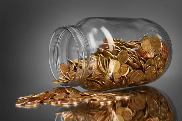 Coins spilling from a money jar on gray background — Stock Photo, Image