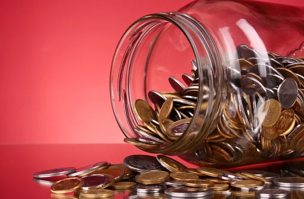 Mynt som rinner från en pengar burk på röd bakgrund — Stockfoto