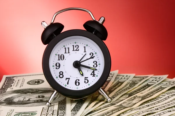 Alarm clock and dollars on red background — Stock Photo, Image