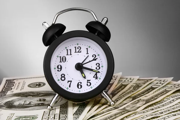 Relógio de alarme e dólares em fundo cinza — Fotografia de Stock