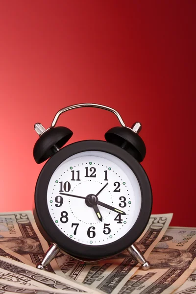 Relógio despertador e dólares no fundo vermelho — Fotografia de Stock