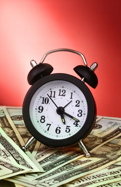Reloj despertador y dólares sobre fondo rojo — Foto de Stock