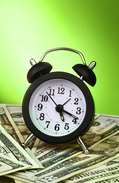 Relógio despertador e dólares em fundo verde — Fotografia de Stock