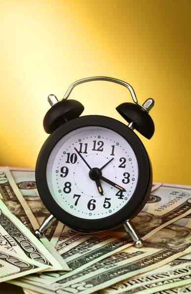 Relógio despertador e dólares em fundo amarelo — Fotografia de Stock