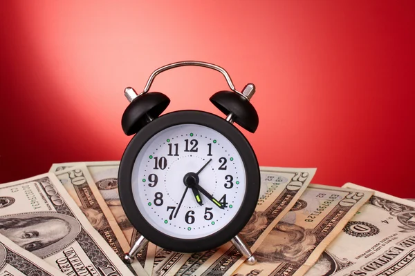 Relógio despertador e dólares no fundo vermelho — Fotografia de Stock