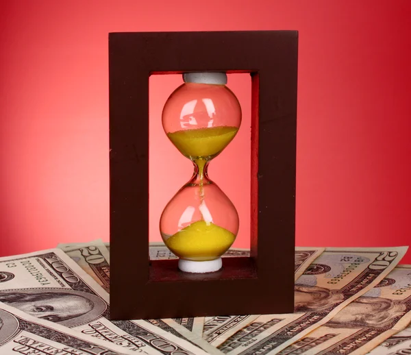 Hourglass and coins on red background — Stock Photo, Image