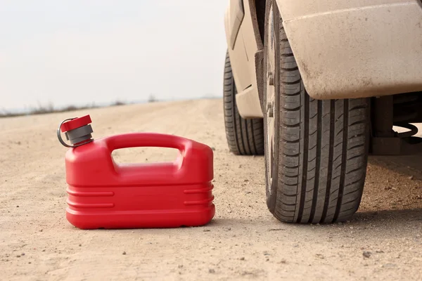 Tanica carburante in plastica rossa su strada sterrata con auto — Foto Stock