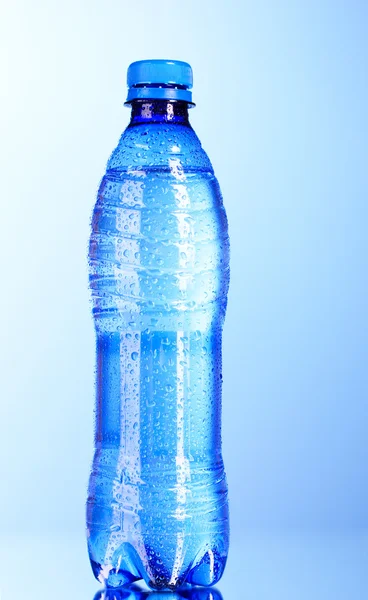 Láhev vody s vodou kapky na modrém pozadí — Stock fotografie