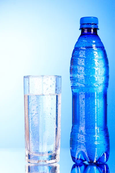 Flasche Wasser mit Glas auf blauem Hintergrund — Stockfoto