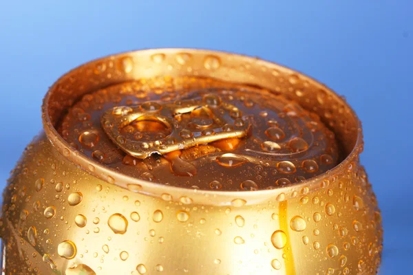 Bière métallique dorée avec gouttes d'eau sur fond bleu — Photo