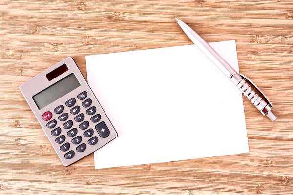 Pen, een vel papier en een rekenmachine op een houten tafel — Stockfoto