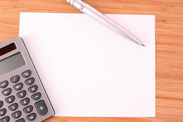 Pen, een vel papier en een rekenmachine op een houten tafel — Stockfoto