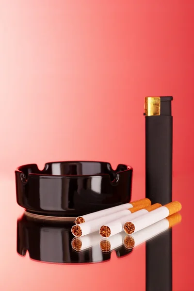 Cigarrillos, cenicero y encendedor sobre fondo rojo —  Fotos de Stock